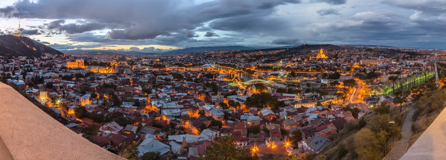 The historic rooftops of Tbilisi glow at dusk beneath a dramatic blue sky