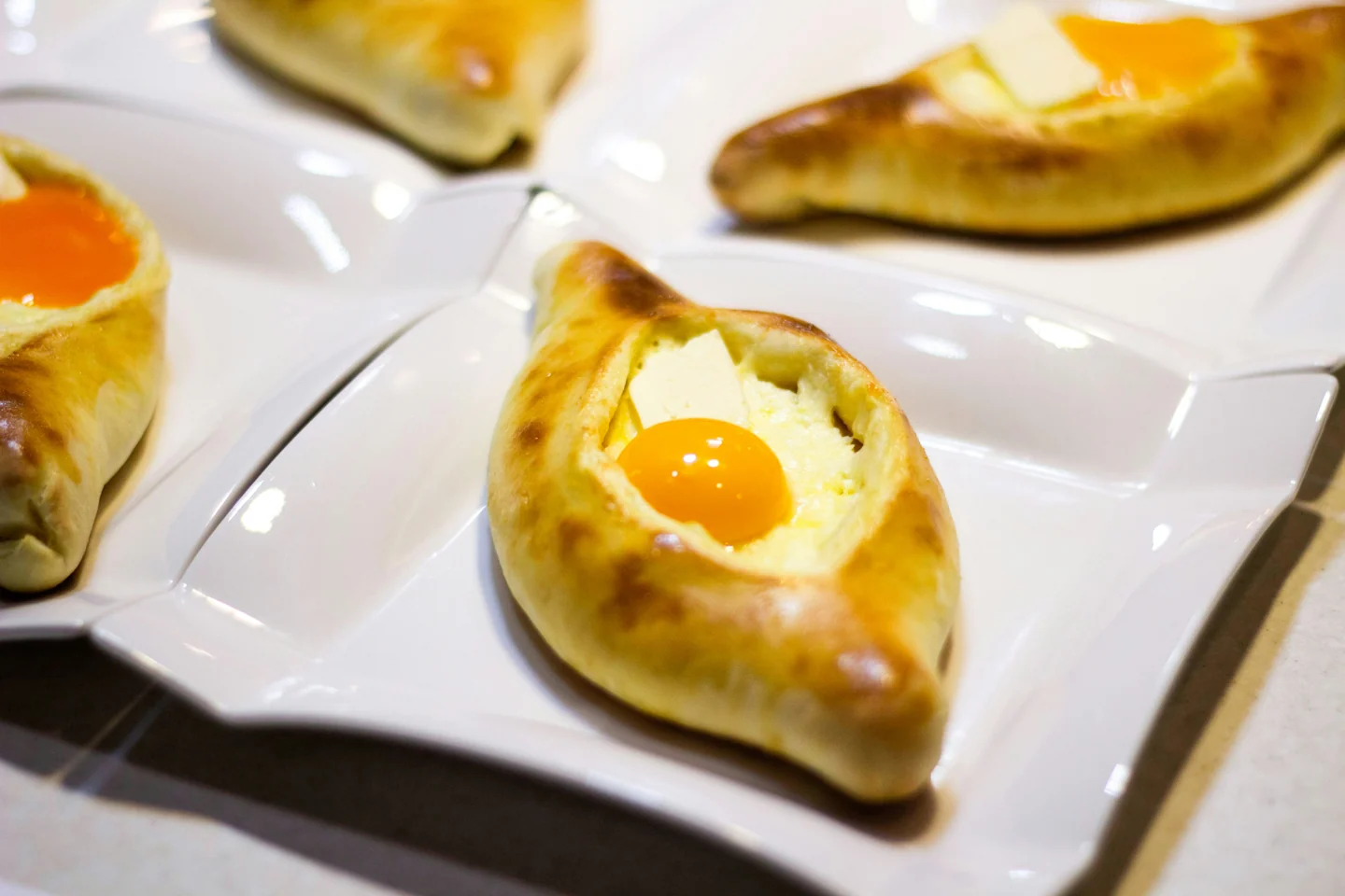 Golden Adjarian khachapuri with cheese, egg yolks and butter on white plates, ready to be served